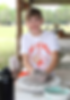 Boy wearing a Camp Stewart uniform outdoors, working on a piece of pottery at a potters wheel