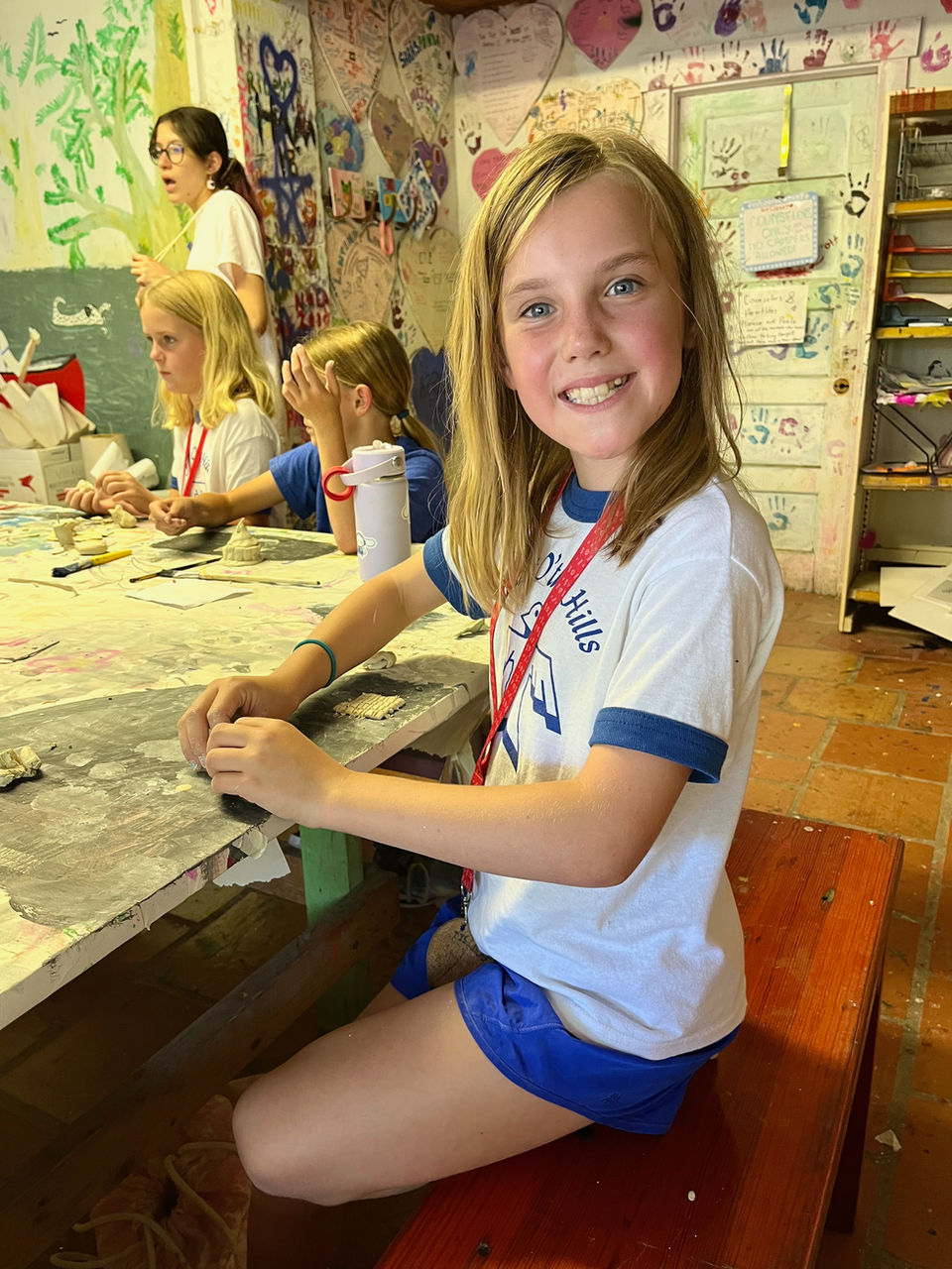 Young blond girl sitting at an arts and crafts table at Heart O' the Hills girls camp.
