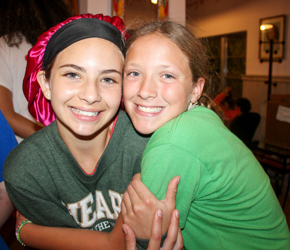Two girls hugging each other, looking at the camera smiling.