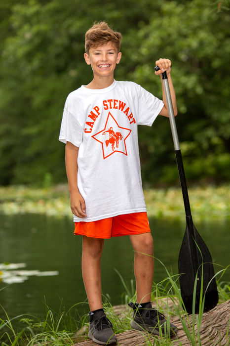 Boy wearing a Camp Stewart uniform standing in next to the river, holding an oar
