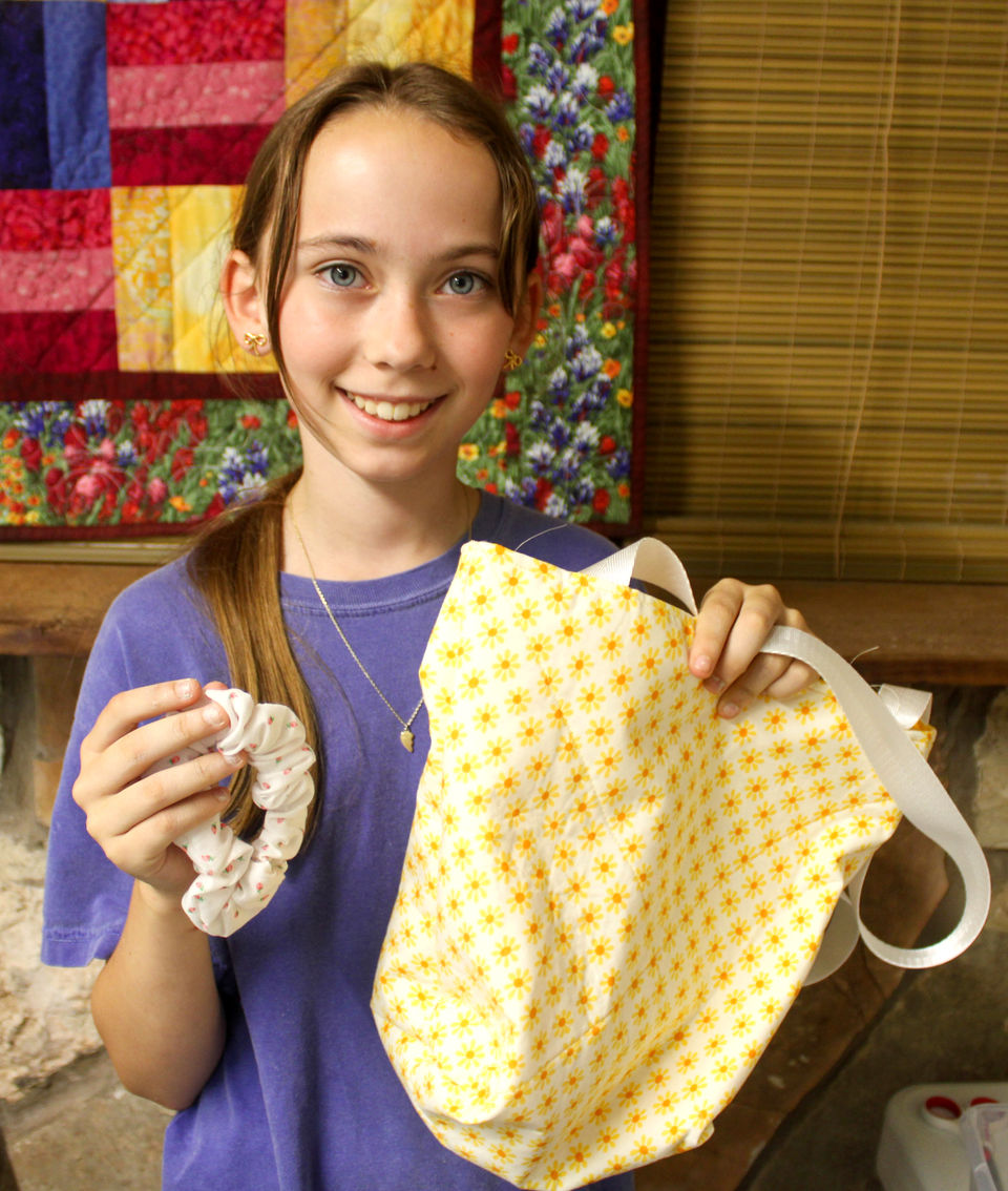 Girl holding up a purse and a scrunchie that she made in a sewing class.