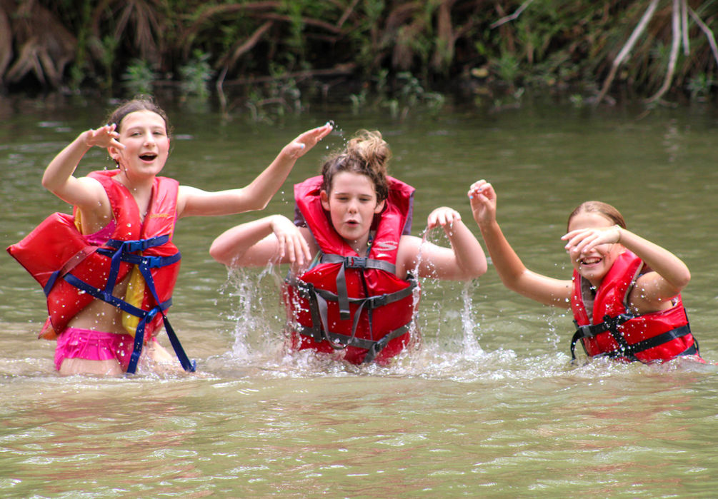 Three girls in red life preservers playing in the river.