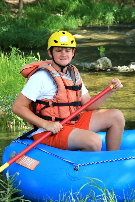Boy sitting in an inflatable kayak on the river, holding an oar