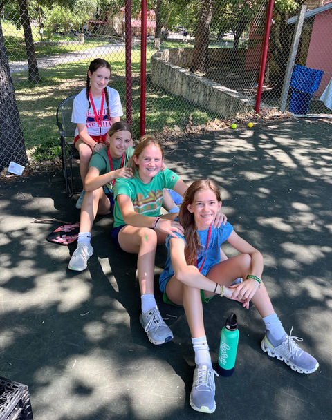 Four girls, each wearing shorts and a t-shirt sitting outdoors looking at the camera and smiling.