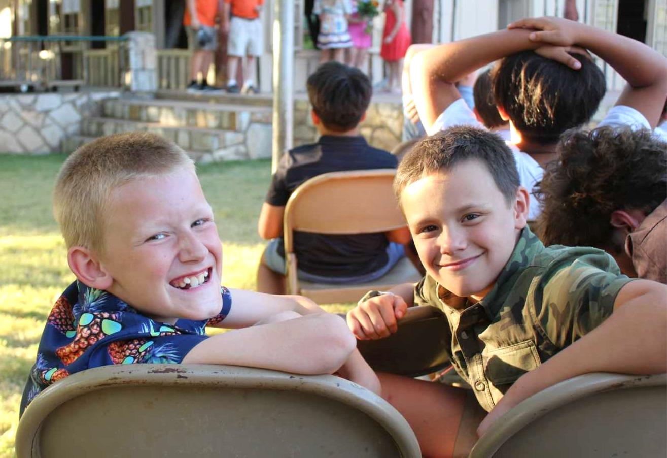 Two boys sitting outdoors facing the camera and smiling