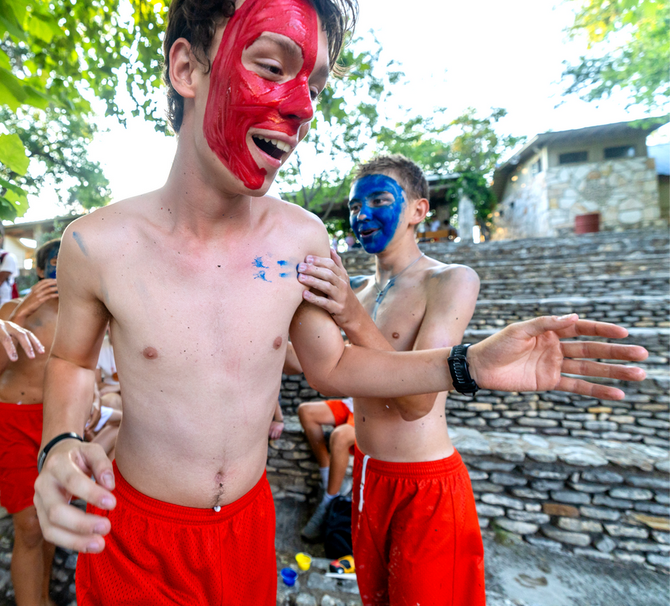 Boys out doors, one wearing red face paint, the other wearing blue face paint