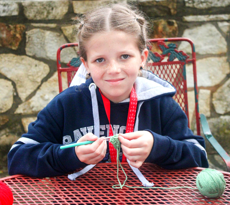 Young girl crocheting with green yarn.