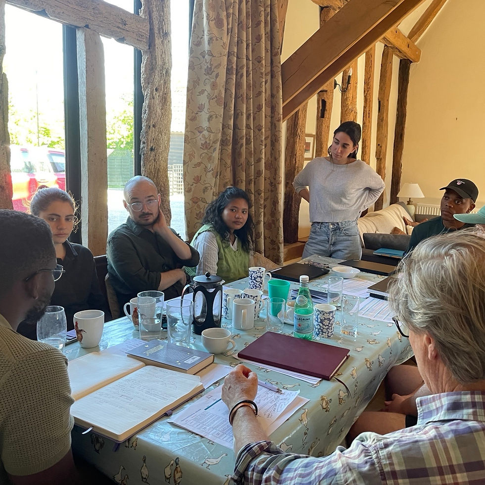 Pema, a Junior WASH Specialist, sits on the left, and Bill, a Senior WASH Specialist, sits on the right. They are seated around a table in the office, reviewing reports on their laptops. Large windows surround them, revealing a view of the quay and a sunset in the background.