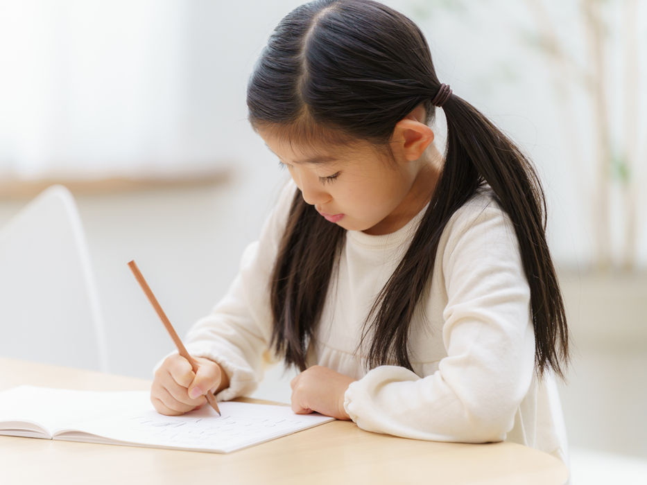 机に向かってノートに鉛筆で書く女の子
