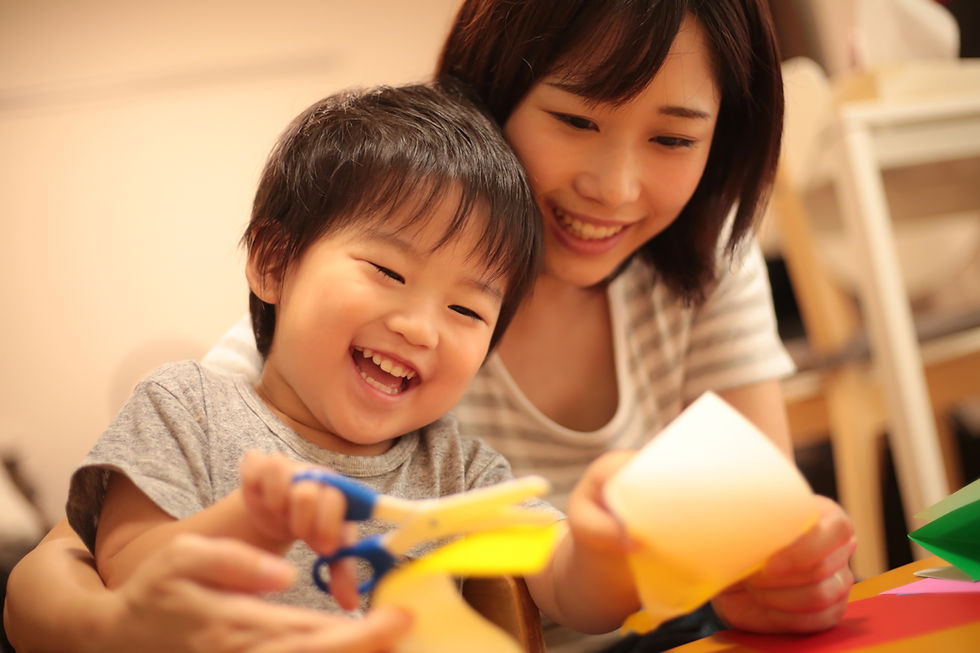 笑顔で折り紙を切る子供と見守る母親