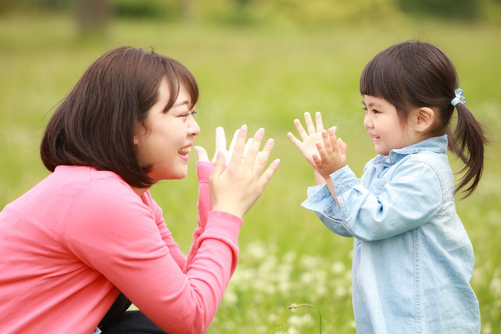 芝生の上で笑顔で手遊びをする母親と小さな女の子