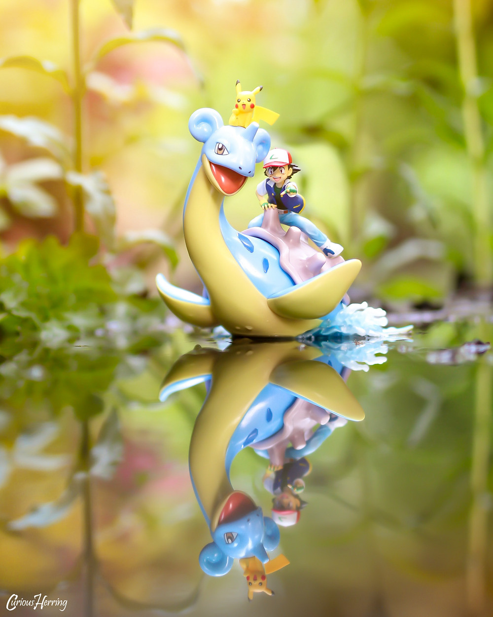 Toy Photography by CuriousHerring of Lapras, Ash and Pikachu swimming across the lake. This image features the G.E.M. Pokemon series statue from Nintendo, using soft focus to blur out the background, with a large focus on the figure and water reflection.