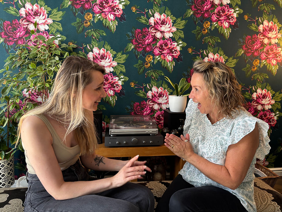 Kirstie and Niki laugh together in front of a floral wall pattern. About Space Between Us