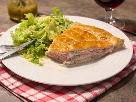 Part de tourte au jambon et champignons servie dans une assiette avec salade verte, pâte feuilletée croustillante