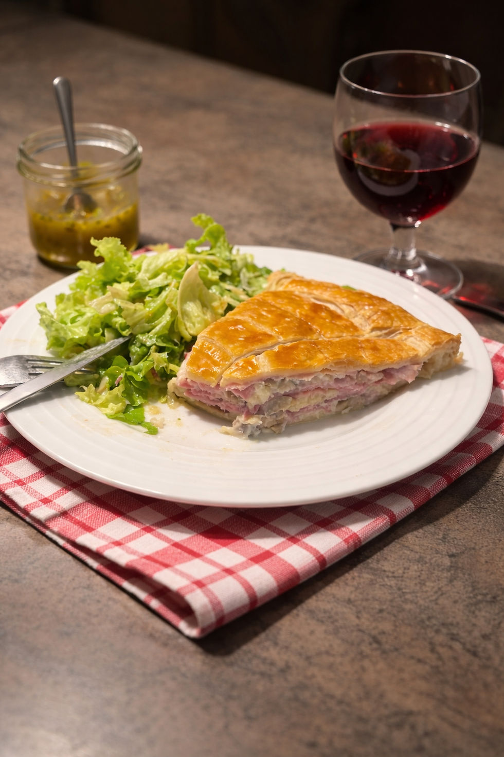 Part de tourte au jambon et champignons servie dans une assiette avec salade verte, pâte feuilletée croustillante