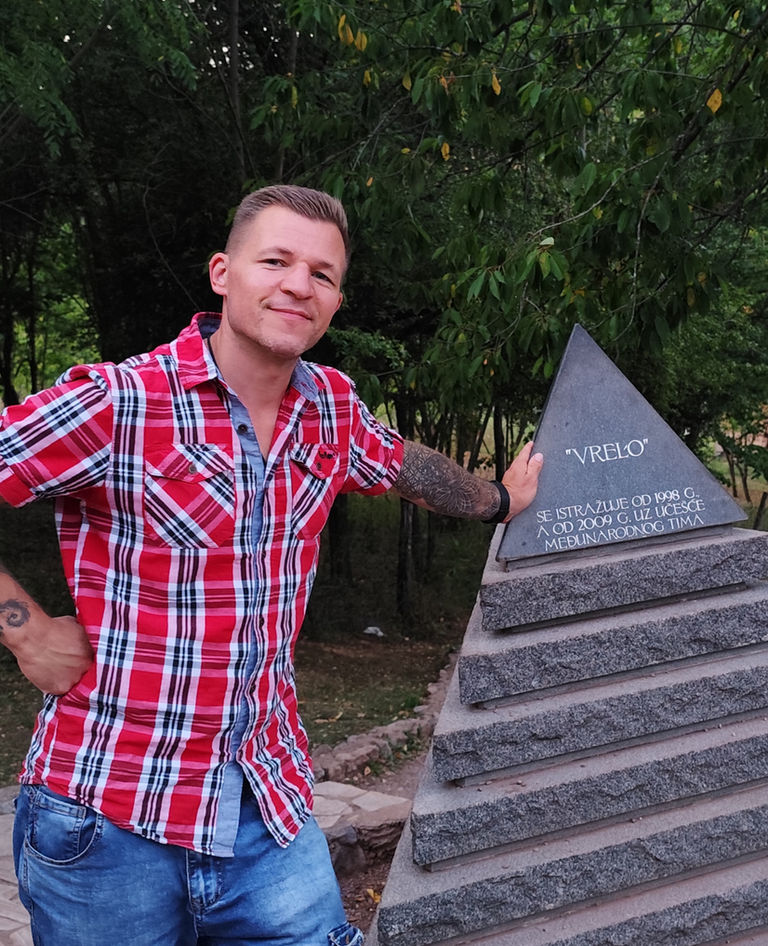 Aleksandar lächelnd vor einem Denkmal