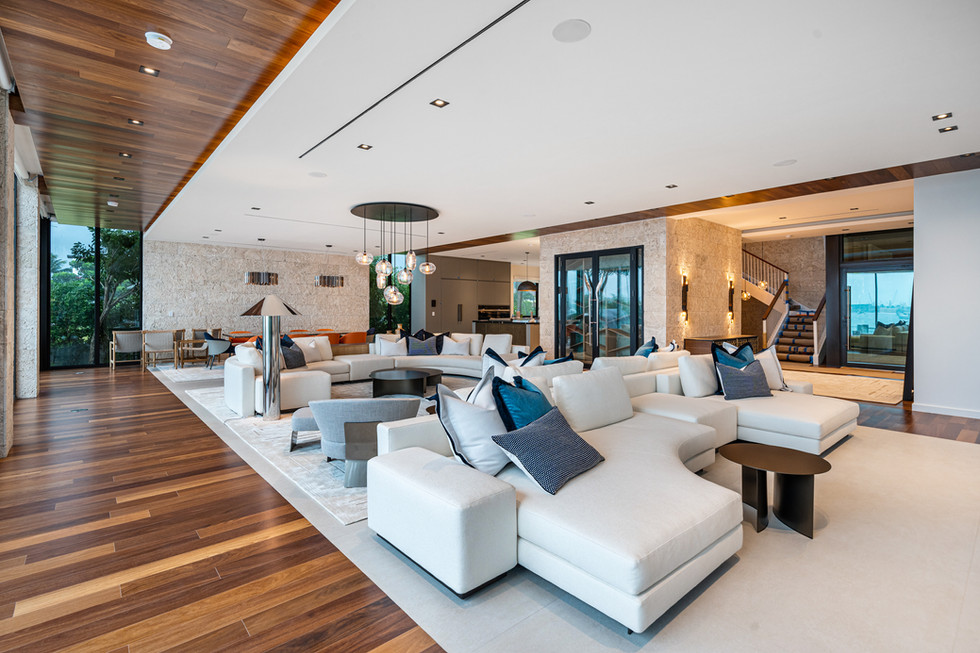 Contemporary living space with white sofas, wood flooring, large windows, and water views in Miami Beach