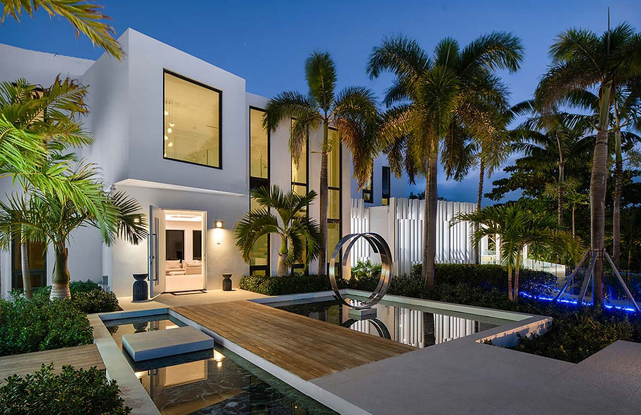 Twilight exterior view of a contemporary urks and Caicos residence with reflecting pool, palm trees, and illuminated entry court