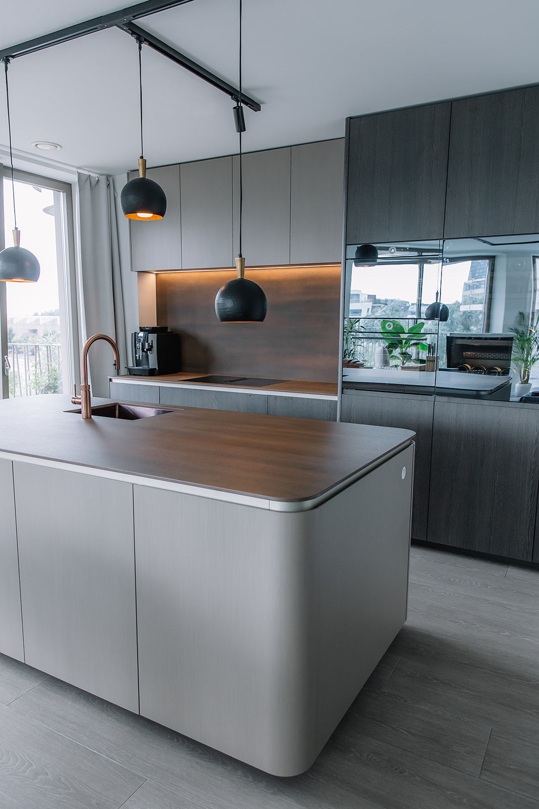 Keuken aan het eilandje in Antwerpen. Als materiaal kozen we voor een hoogwaardig houtlaminaat met een opvallende nerfstructuur. Werkbladen keramisch van het merk laminam. Een rose quooker kraan en vzug toestellen.