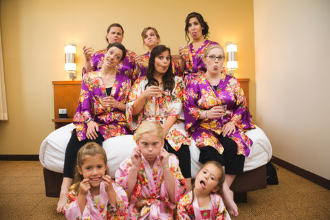 Bride, all her attendants, and flower girls making funny faces at the camera, while getting ready