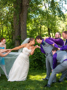 Wedding Party playfully tugging bride and groom away from each other, while they try to kiss