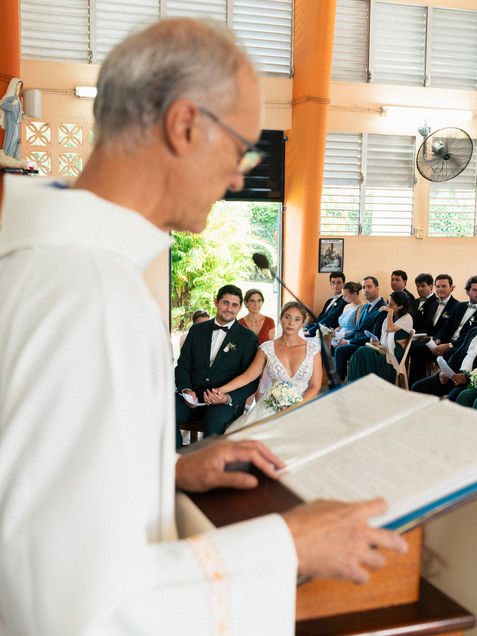 Cérémonie de mariage à l’église avec les mariés attentifs pendant la lecture du prêtre entourés de leurs proches.