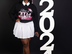 Senior portrait photography in Dallas Fort Worth featuring Class of 2024 graduate in cap and sweatshirt standing beside large numbers in Bedford Texas studio.