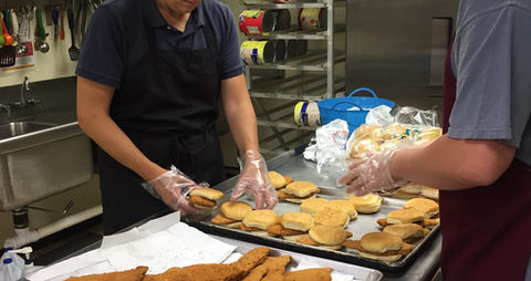 Two people organizing and assembling chicken sandwiches to be served to soup kitchen guests.