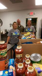 Three volunteers standing behind boxes of food being checked into and organized at the food pantry.
