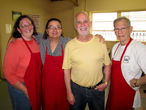 Group of four volunteers, three of which are in red aprons, smiling at the camera.