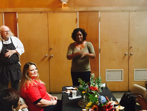 Woman standing behind table, giving a speech, at a volunteer award ceremony.