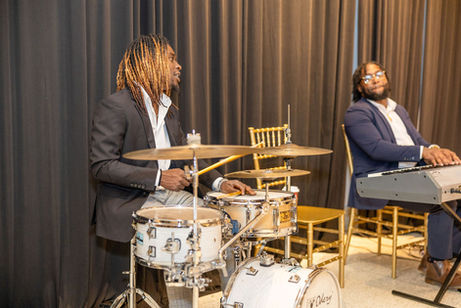 A man playing drums next to a man playing the keyboard on stage at the Power of the Plate Gala