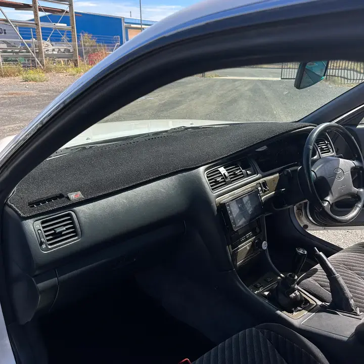 Black dashboard mat in a white car interior with a steering wheel, gear shift, and air vents visible.