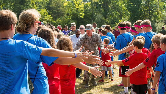 smiling united states veterans walking through two sides of young people in red and blue t-shits touching hands as they go