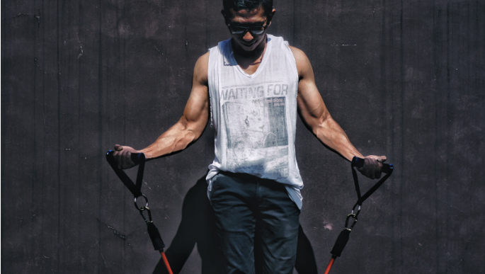 A guy flexes his arm muscles while using TRX.