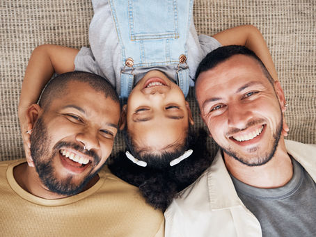 Three smiling family members lie head-to-head on a woven rug, with a child upside down between two men.