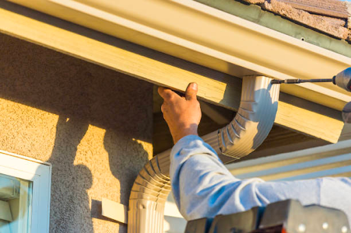 A man fixing a gutter with a power drill.