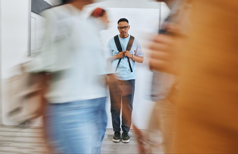 Young man with glasses stands still in a hallway while blurred people pass in front of him