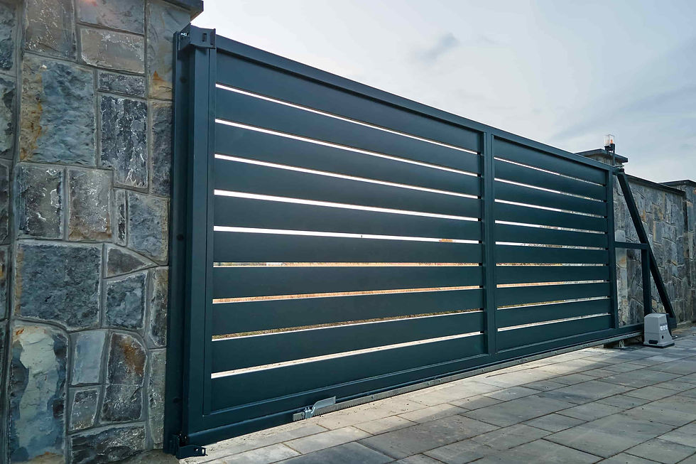 Dark teal sliding driveway gate with stone pillars and paved patio under a cloudy sky.