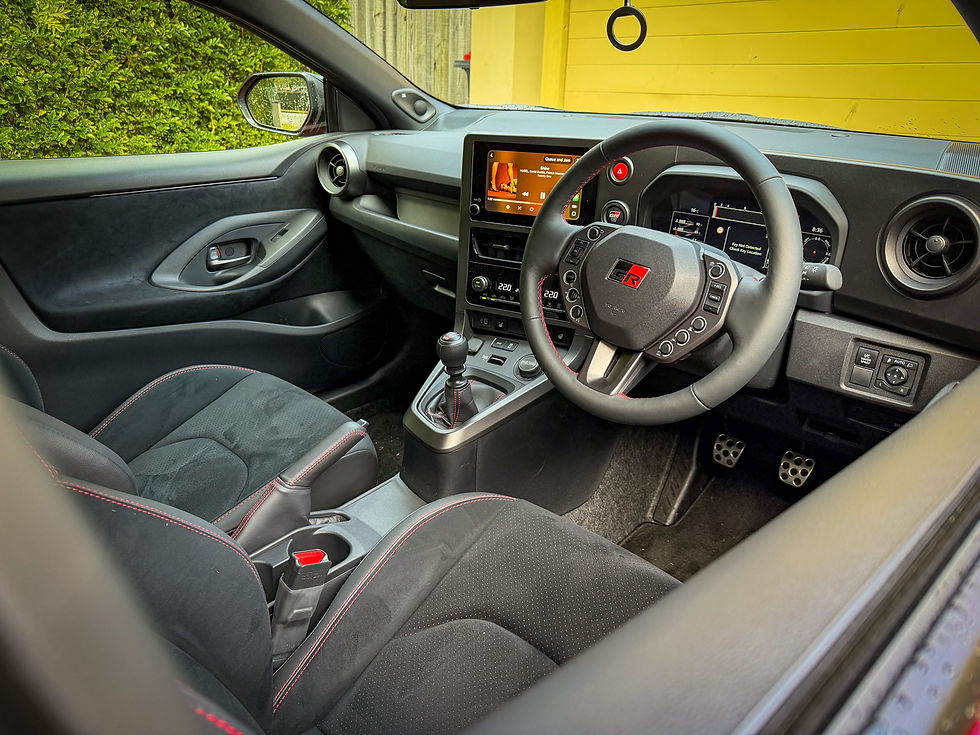 Empty Toyota GR car interior with manual gearshift, steering wheel, digital dash, and yellow wall outside.