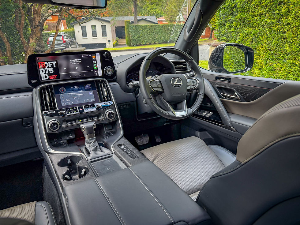 Lexus SUV interior with steering wheel and dual screens playing music, black leather seats, parked on a leafy suburban street.