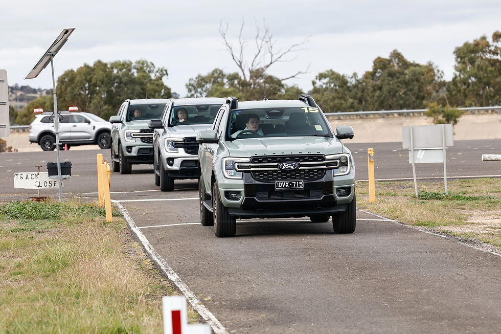 Three Ford SUVs line up on a test track, driver visible in front vehicle, with TRACK CLOSE sign and trees under cloudy sky.