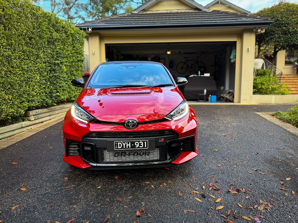Red Toyota GR Yaris parked in a suburban driveway, with open garage behind and license plate DYH 931 visible.