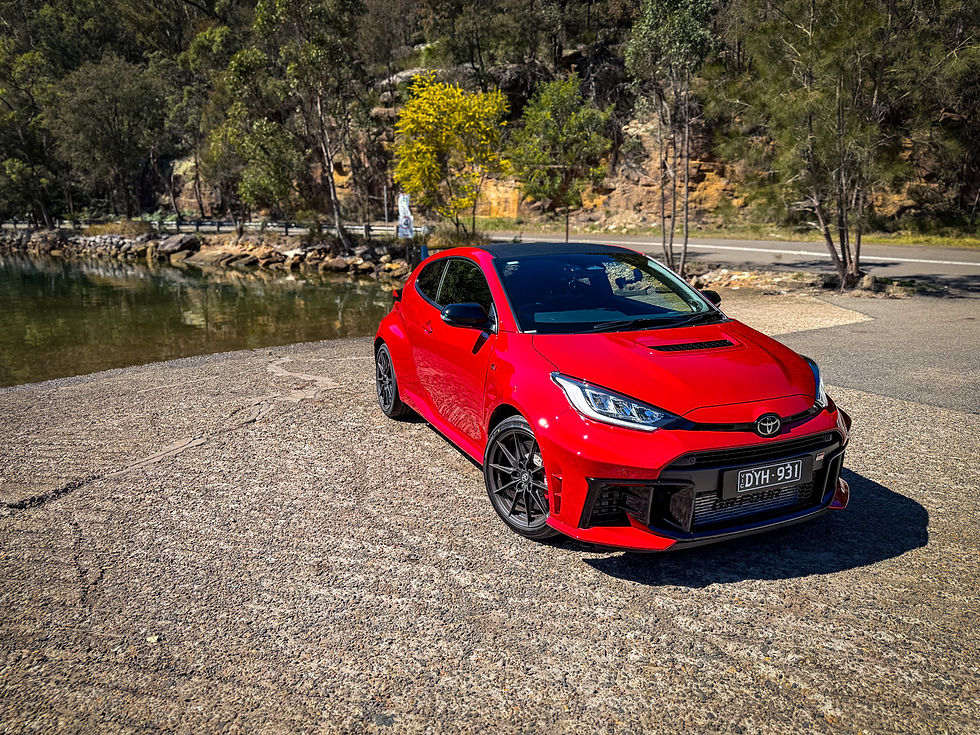 Red Toyota sports car parked by a river on a wooded roadside, with license plate DYH 931.