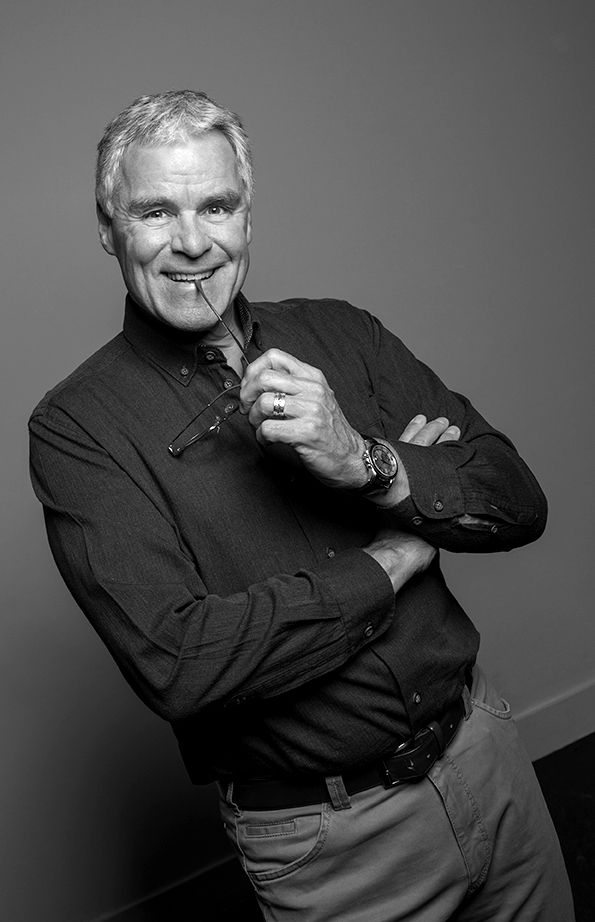 Man smiling while holding glasses; grey background; professional headshot of him.