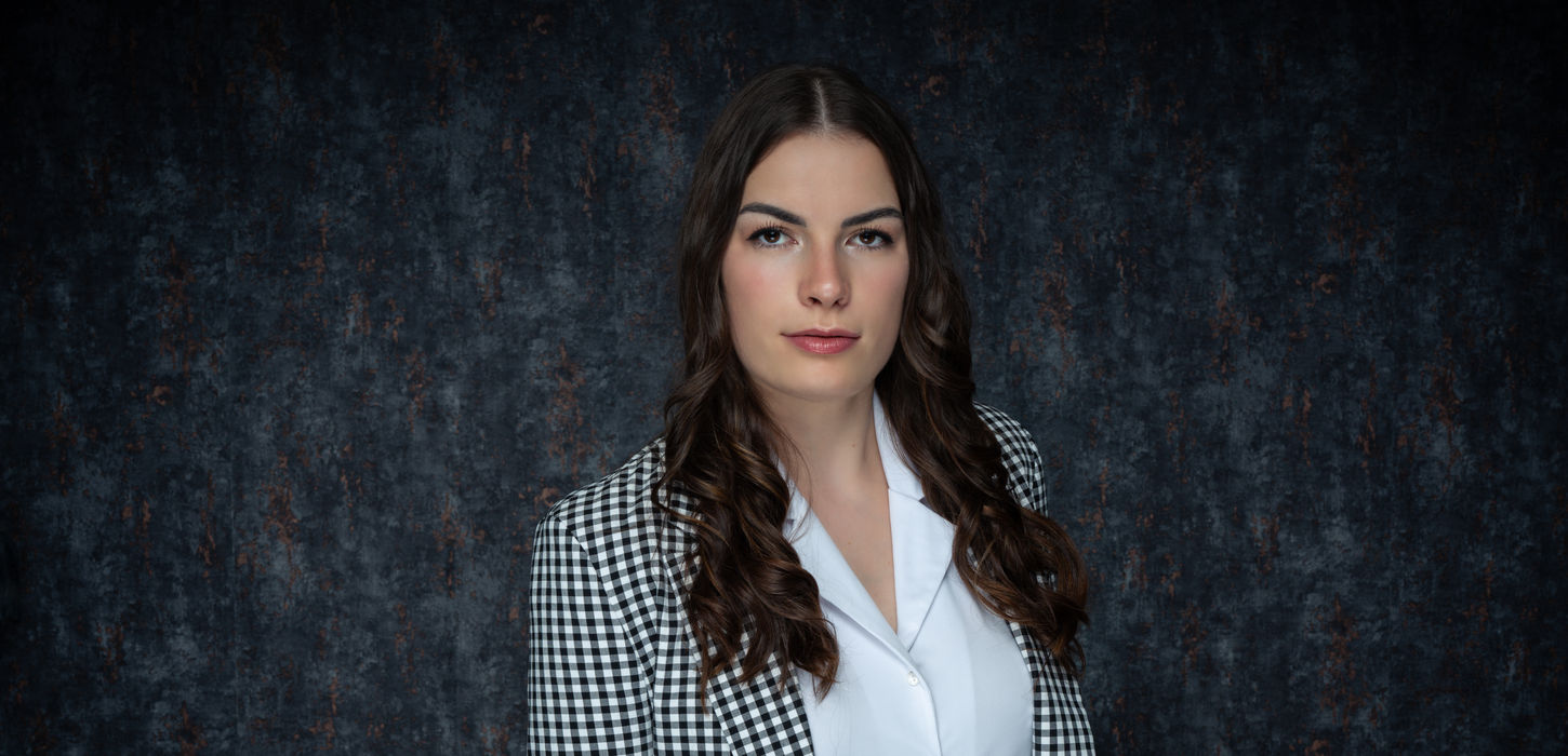 Professionelles Businessporträt einer jungen Frau mit langen Haaren im karierten Blazer vor dunklem Studiohintergrund in Illingen, Baden-Württemberg.