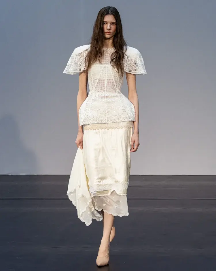 A model is wearing a white slik and lace skirt and top