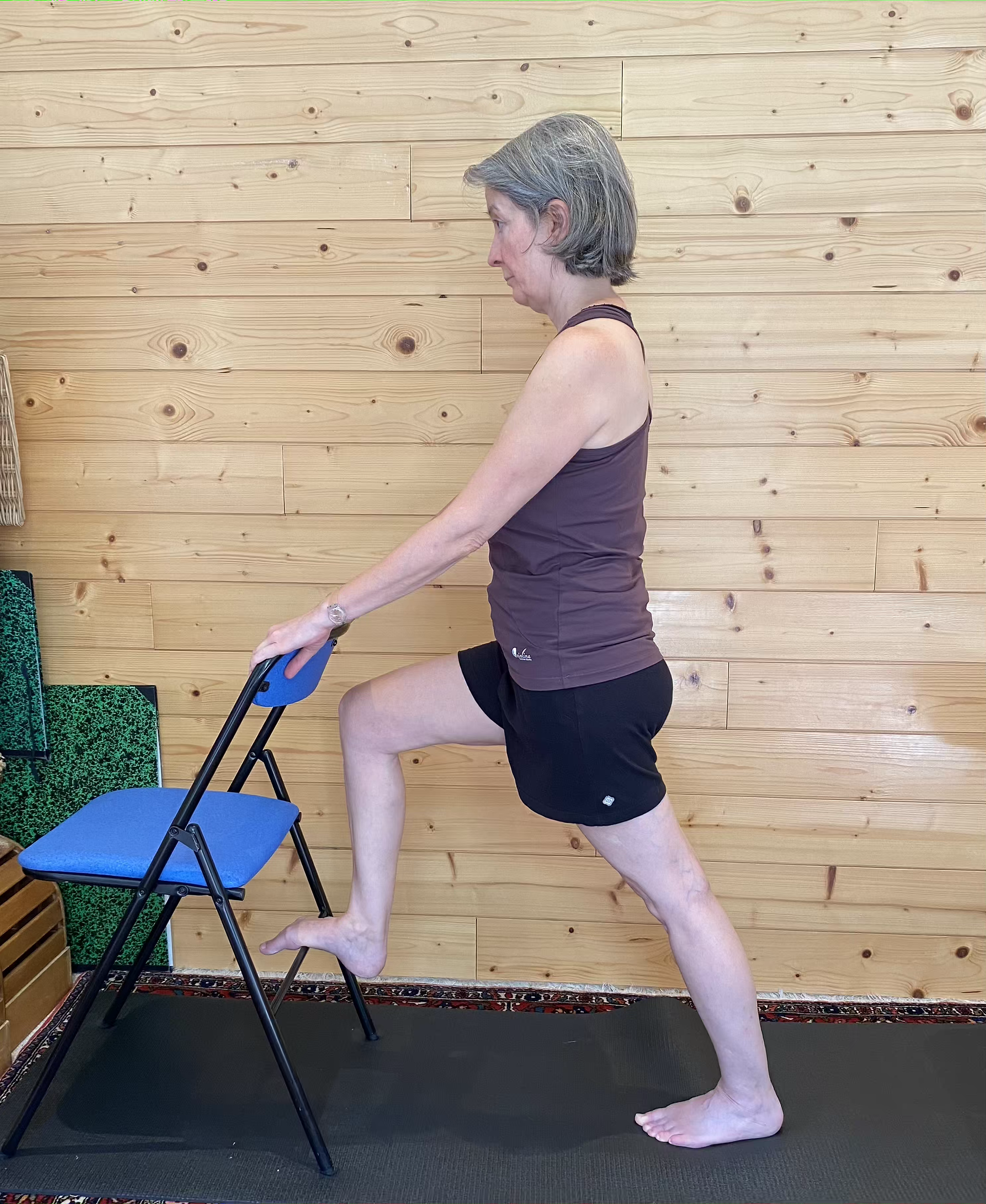 Cath en short noir et maillot violine, travaille ses jambes avec une chaise