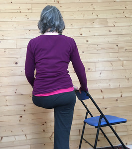 Vue de dos, Cath a placé le pied gauche sur le dossier de la chaise