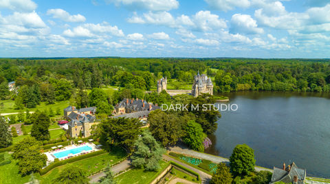 Vue aérienne ensoleillée du Château de la Bretesche bordé par son grand étang et la végétation dense de la forêt de Brière en Loire-Atlantique.